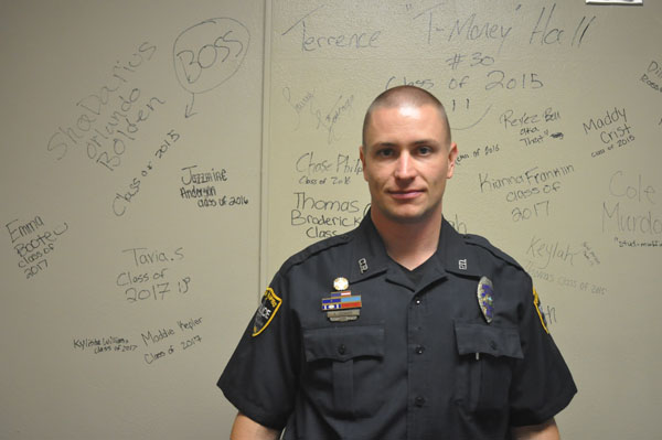 School Resource Officer Aaron Leisinger in Officer Hansels office in front of a board full of messages left by students for Hansel.