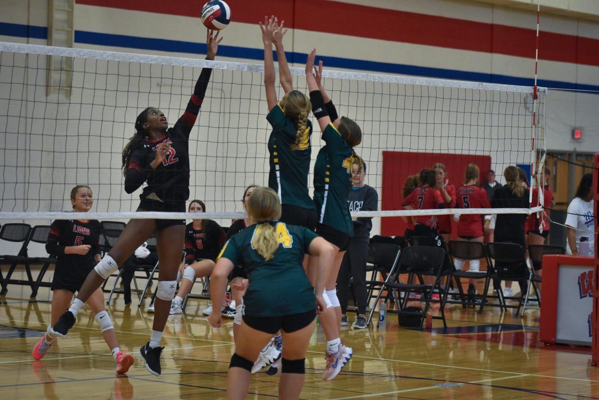 Freshmen Liv Boedeker and Scarlet Lang attempting to block the ball from coming over the net.