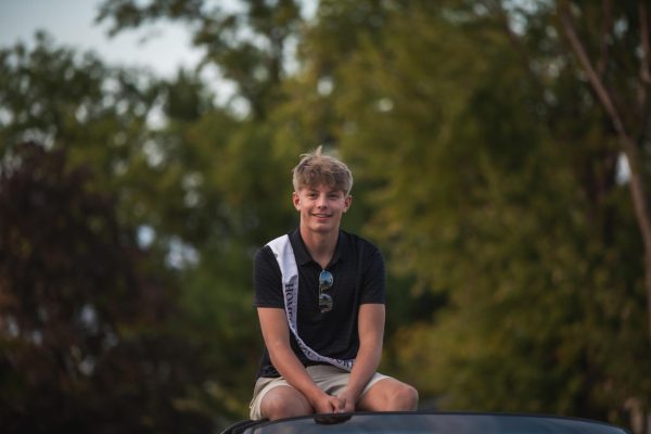 Smiling at the camera, senior homecoming court nominee Jace Scott sits on top of a Corvette. 