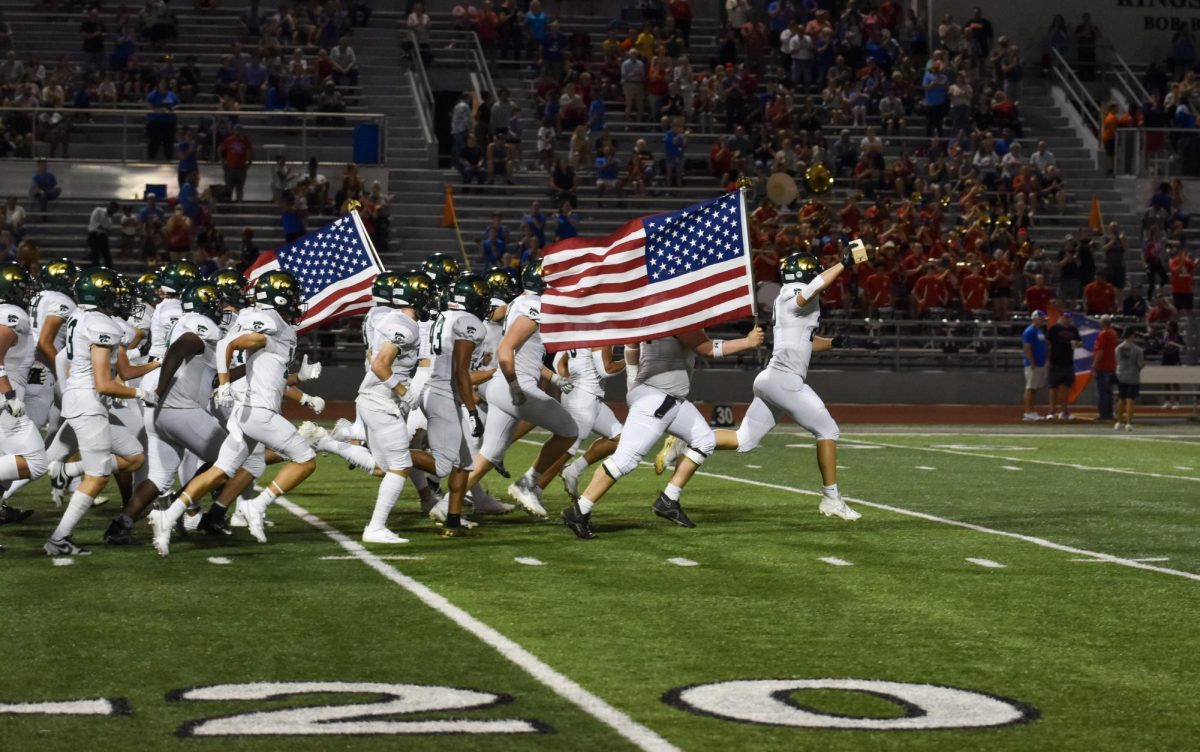 Kennedy Varsity Football kicks off the game with the traditional run onto the field with the American flag.