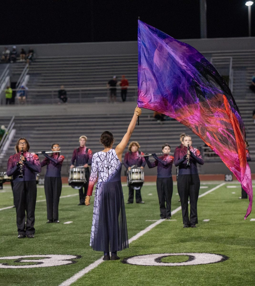 Senior Karen Garcia stands facing the band as she holds her flag high.