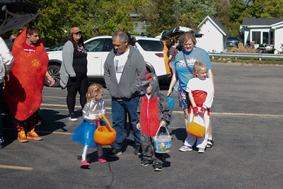 Escorted by adults, children walk to cars at Trunk-or-Treat, asking for candy. 