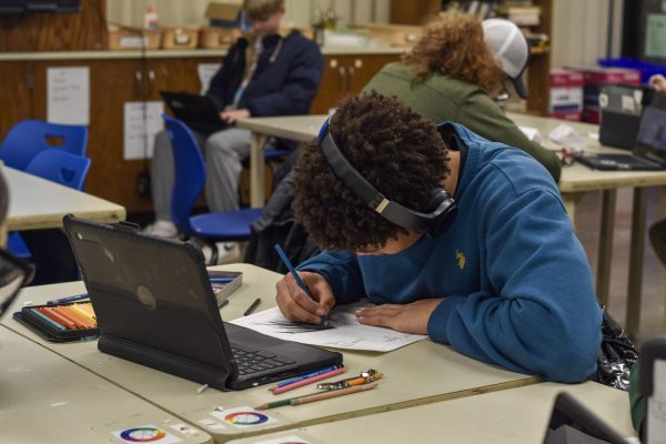 Listening to music, junior Gavin Grant focuses on his art piece referring to an image on his Chromebook.